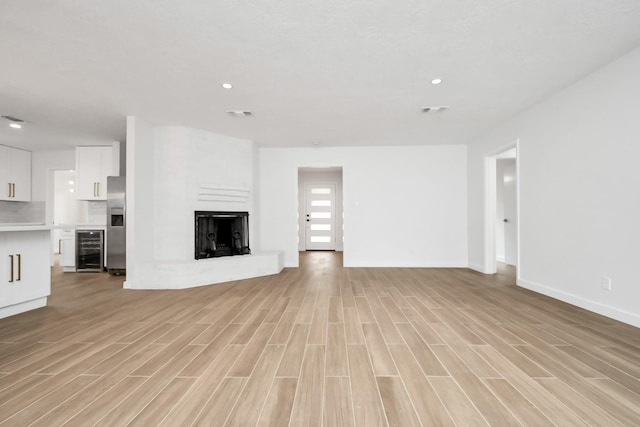 unfurnished living room with wine cooler, light wood-style flooring, visible vents, and a fireplace with raised hearth