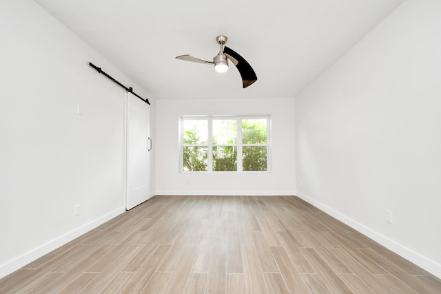 spare room with a barn door, baseboards, light wood-style floors, and a ceiling fan