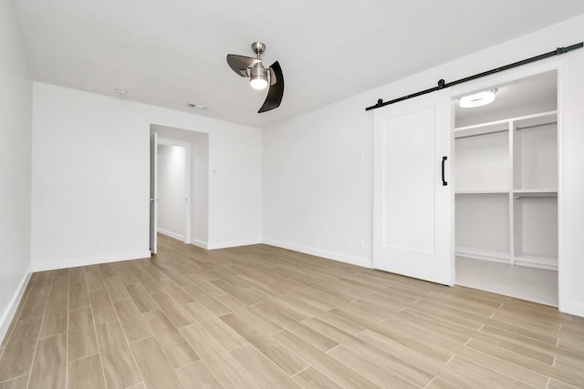 unfurnished bedroom with a ceiling fan, baseboards, visible vents, a barn door, and light wood-type flooring