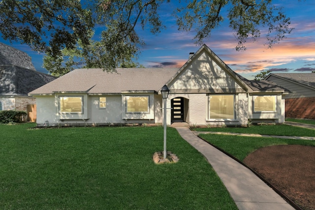 view of front of house featuring brick siding, a lawn, and roof with shingles