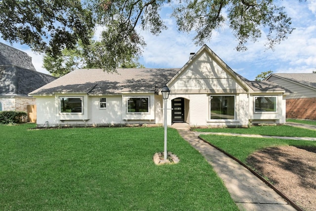 view of front of house with brick siding, a chimney, a front yard, and roof with shingles