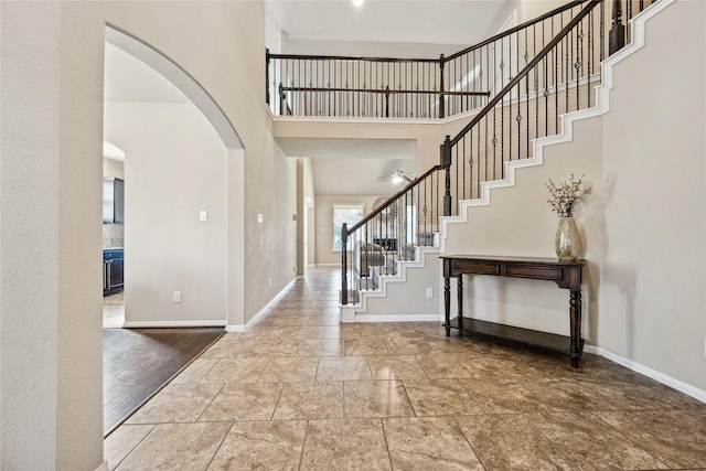 entrance foyer featuring baseboards, stairway, a towering ceiling, arched walkways, and a ceiling fan