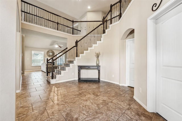 foyer featuring arched walkways, stairway, baseboards, and ceiling fan