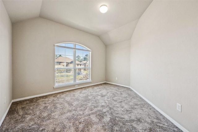 carpeted empty room featuring vaulted ceiling and baseboards