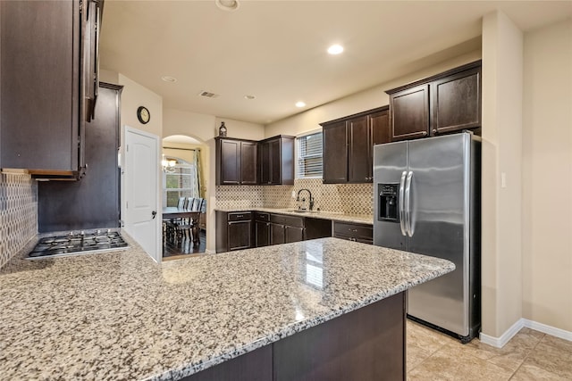 kitchen featuring light stone counters, backsplash, dark brown cabinetry, appliances with stainless steel finishes, and a peninsula