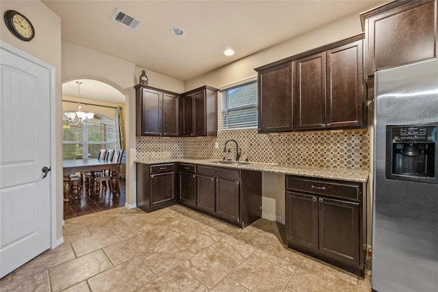 kitchen featuring stainless steel fridge with ice dispenser, a sink, dark brown cabinets, a notable chandelier, and tasteful backsplash