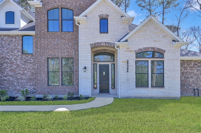 french country style house with a front lawn, brick siding, and stone siding