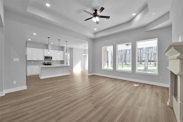 unfurnished living room featuring light wood-type flooring, a raised ceiling, baseboards, and a fireplace