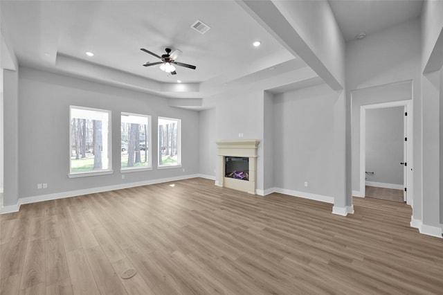 unfurnished living room with visible vents, baseboards, light wood-style flooring, a fireplace, and a raised ceiling