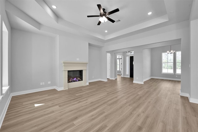 unfurnished living room with a glass covered fireplace, a raised ceiling, light wood-style floors, and baseboards