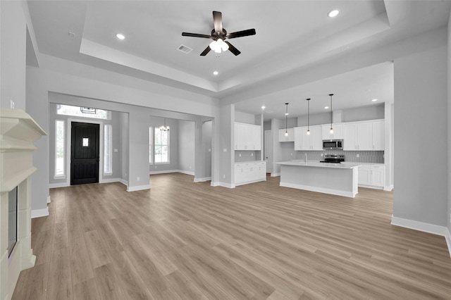 unfurnished living room with visible vents, light wood-style flooring, and a tray ceiling