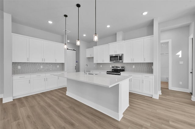 kitchen featuring light wood-type flooring, light countertops, a barn door, stainless steel appliances, and a sink