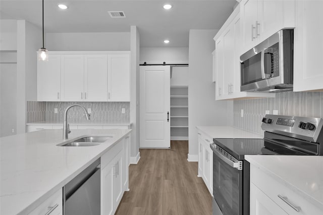 kitchen featuring visible vents, a sink, white cabinetry, stainless steel appliances, and a barn door