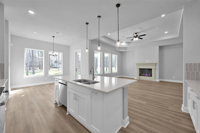 kitchen featuring light wood-type flooring, a sink, a tray ceiling, a fireplace, and light countertops