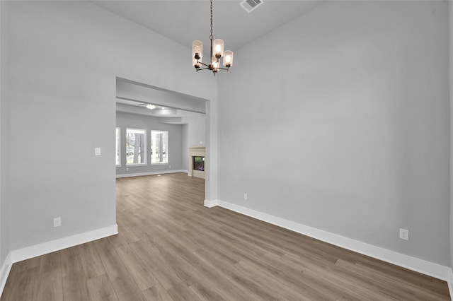 empty room featuring visible vents, wood finished floors, a glass covered fireplace, baseboards, and a chandelier