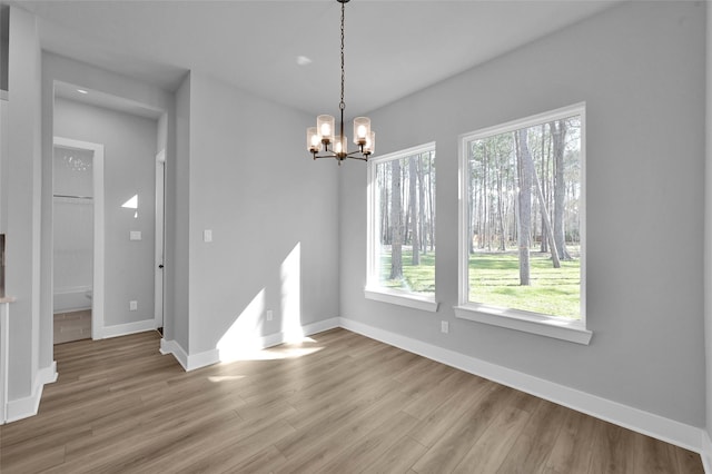 unfurnished dining area with baseboards, plenty of natural light, an inviting chandelier, and wood finished floors