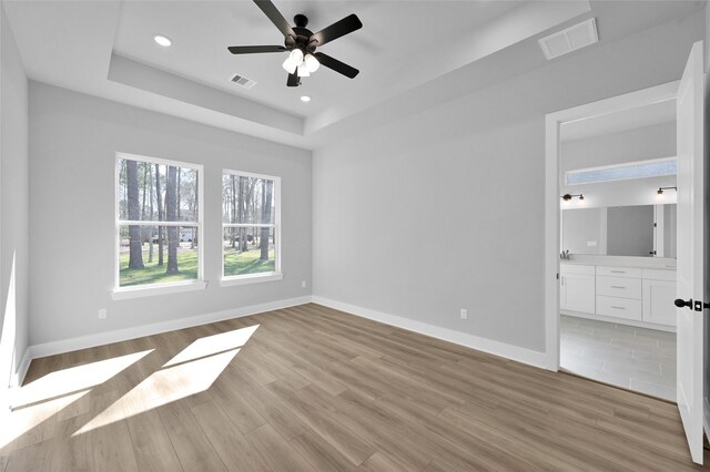 unfurnished bedroom featuring visible vents, baseboards, recessed lighting, light wood-style floors, and a raised ceiling