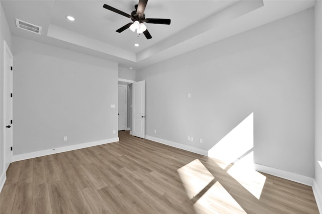 unfurnished bedroom featuring visible vents, baseboards, light wood-type flooring, a tray ceiling, and recessed lighting