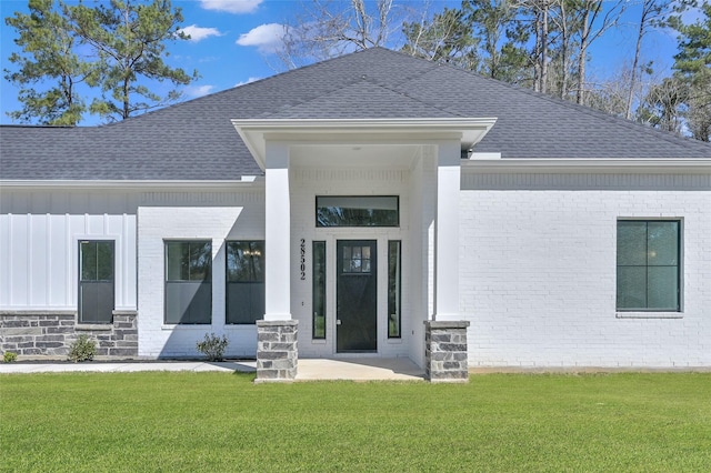 doorway to property featuring a yard, board and batten siding, brick siding, and roof with shingles