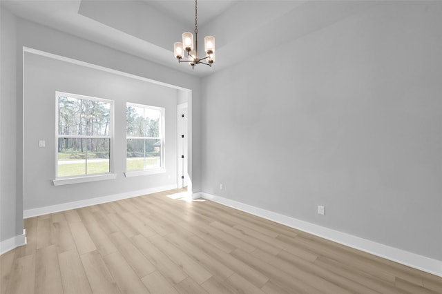 spare room featuring baseboards, light wood-style floors, and an inviting chandelier