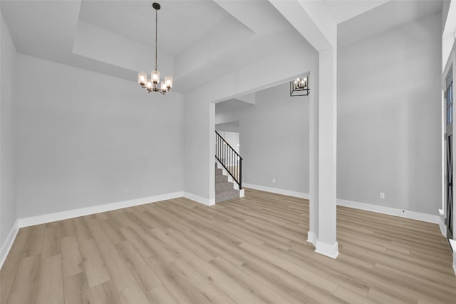 unfurnished dining area with baseboards, a chandelier, stairs, light wood-style flooring, and a raised ceiling