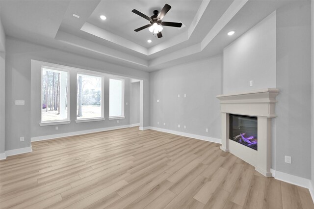 unfurnished living room with light wood-type flooring, a raised ceiling, baseboards, and a glass covered fireplace