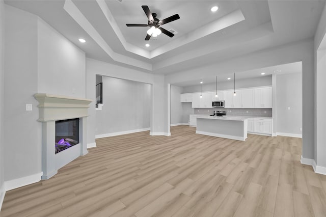 unfurnished living room with a raised ceiling, light wood-style floors, and baseboards