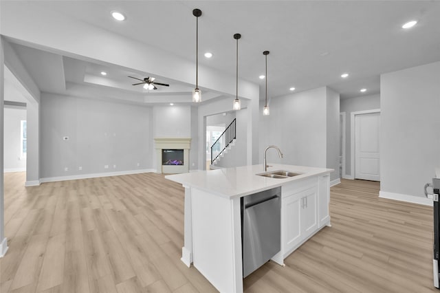 kitchen with a sink, light countertops, a glass covered fireplace, white cabinetry, and stainless steel dishwasher