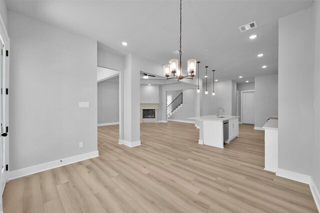 interior space with visible vents, light wood-type flooring, recessed lighting, a glass covered fireplace, and a sink