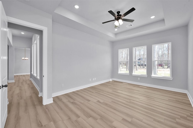 empty room featuring visible vents, light wood-type flooring, a tray ceiling, recessed lighting, and baseboards