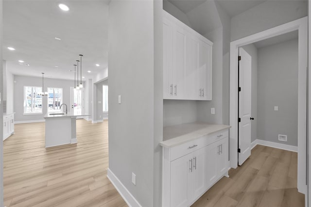 hall featuring light wood finished floors, recessed lighting, an inviting chandelier, and baseboards