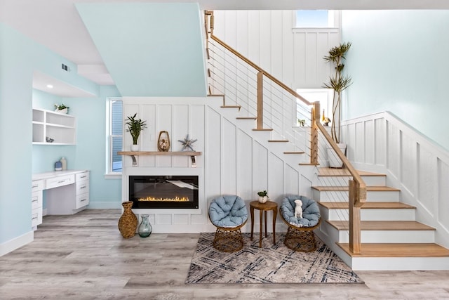 staircase with a glass covered fireplace, built in desk, visible vents, and wood finished floors