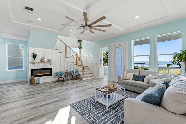 living room with plenty of natural light, stairs, a glass covered fireplace, and wood finished floors