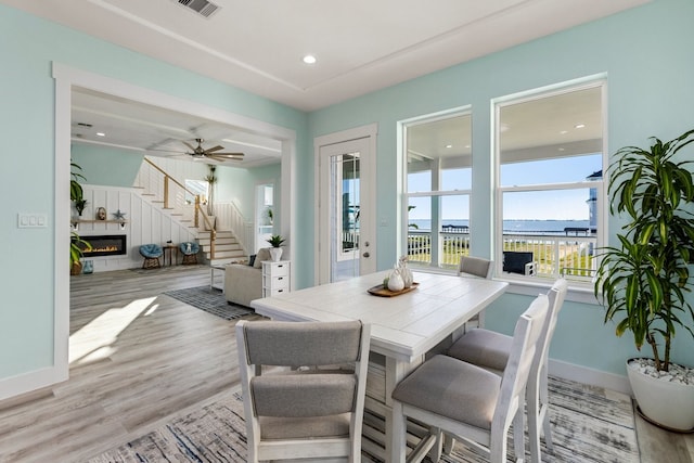 dining space featuring visible vents, baseboards, stairway, light wood-type flooring, and a glass covered fireplace