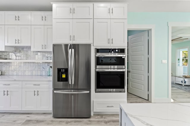 kitchen featuring tasteful backsplash, light wood-type flooring, light stone counters, appliances with stainless steel finishes, and white cabinetry