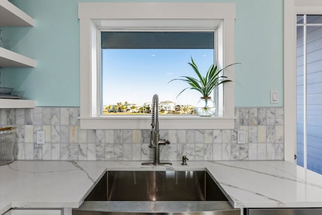 kitchen with open shelves, light stone countertops, tasteful backsplash, and a sink