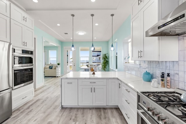 kitchen featuring tasteful backsplash, appliances with stainless steel finishes, a peninsula, white cabinetry, and wall chimney exhaust hood