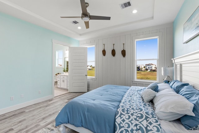 bedroom featuring light wood finished floors, visible vents, baseboards, and a tray ceiling