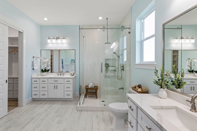 full bath with two vanities, wood finished floors, a stall shower, and a sink