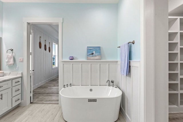 full bath featuring vanity, wood finished floors, wainscoting, and a freestanding bath