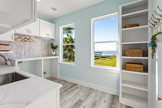 kitchen with a water view, a sink, tasteful backsplash, white cabinets, and light wood finished floors