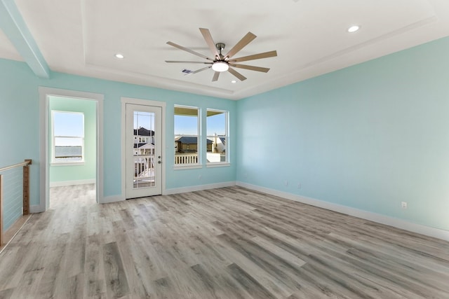 empty room featuring a ceiling fan, a tray ceiling, recessed lighting, light wood-style floors, and baseboards