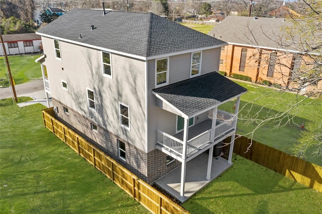 rear view of property with a yard, a patio, roof with shingles, and fence