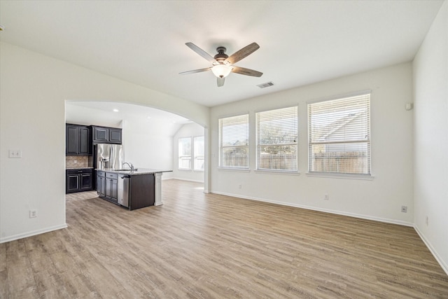 unfurnished living room featuring light wood-type flooring, visible vents, a ceiling fan, a sink, and arched walkways