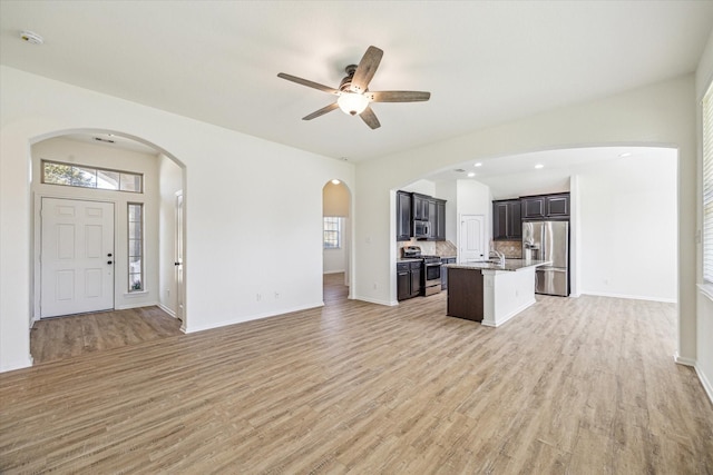 unfurnished living room with a ceiling fan, baseboards, light wood finished floors, and a sink