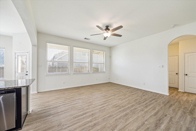 unfurnished living room featuring visible vents, light wood-style flooring, a ceiling fan, arched walkways, and baseboards