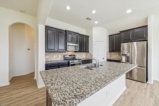 kitchen with visible vents, light wood finished floors, arched walkways, a sink, and stainless steel appliances