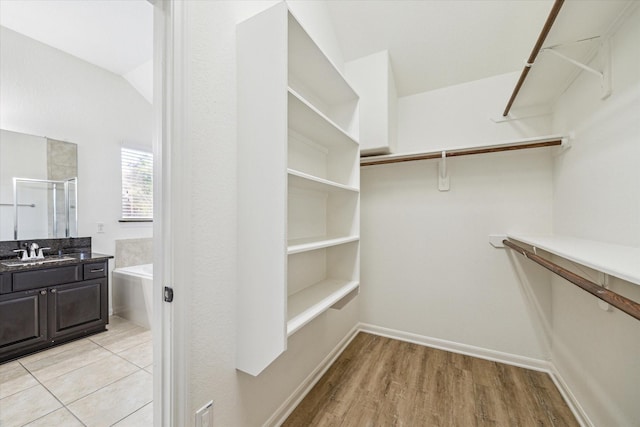 walk in closet with lofted ceiling, light wood-style flooring, and a sink