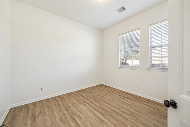 spare room with light wood-type flooring, visible vents, and baseboards