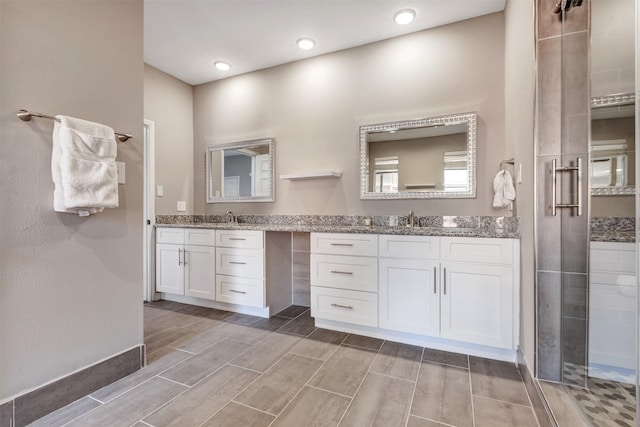 full bath with a sink, tiled shower, and two vanities